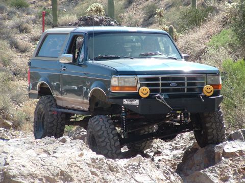 1990 Ford Bronco - A modified Ford Bronco tackles a challenging off-road trail in a desert environment.