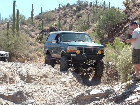 1990 Ford Bronco - A modified Ford Bronco tackles a challenging off-road course in a desert landscape.