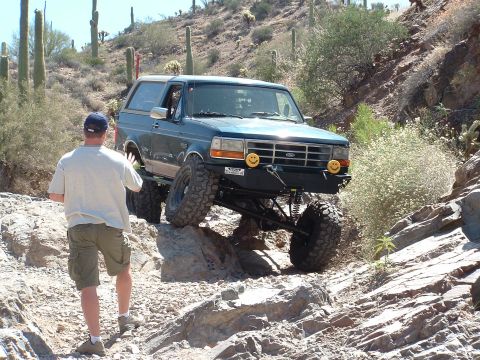 1990 Ford Bronco - A 1990 Ford Bronco tackles a challenging off-road course in a desert landscape.