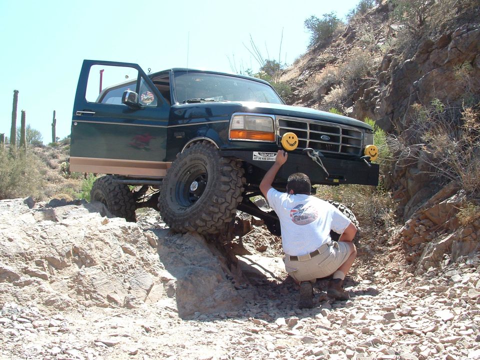Man adjusting smiley face light on front bumper of lifted Ford F-Series truck on rocky off-road trail