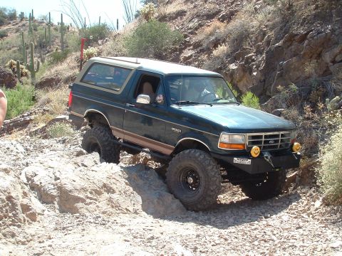 1990 Ford Bronco - A dark green 1990 Ford Bronco tackles a challenging rocky trail during an off-road excursion.