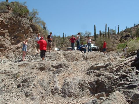 1990 Ford Bronco - A group of people stand around a white 1990 Ford Bronco in a desert canyon.