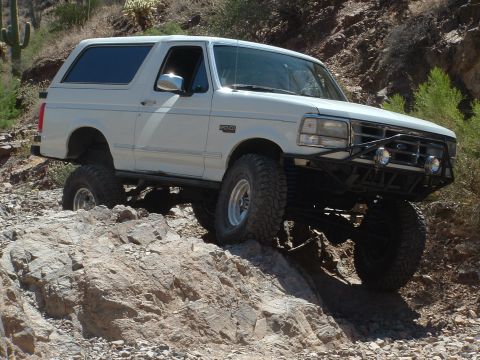 1990 Ford Bronco - White 1990 Ford Bronco navigating a rocky trail with lifted suspension.