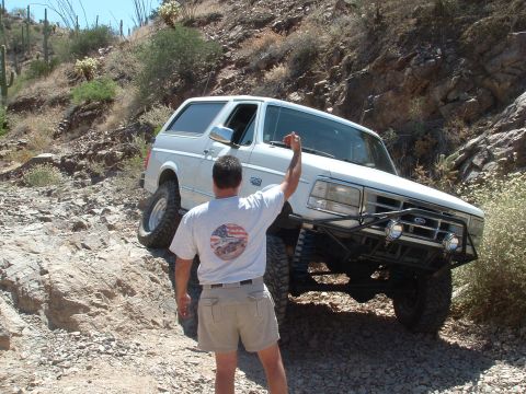 1990 Ford Bronco - A white Ford Bronco navigates a steep, rocky trail in a desert environment.