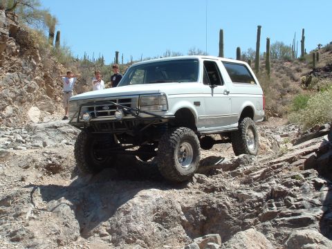 1990 Ford Bronco - A white 1990 Ford Bronco tackles a challenging rocky terrain on an off-road adventure.