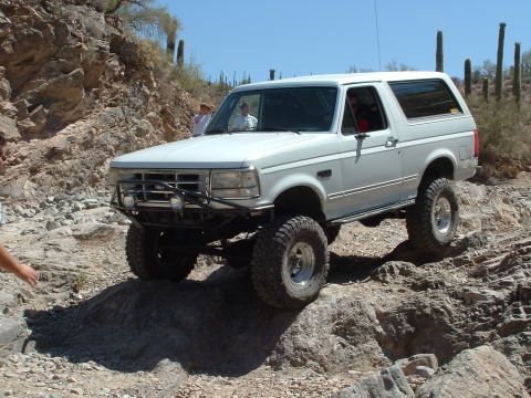 1990 Ford Bronco - White 1990 Ford Bronco navigates a challenging rocky terrain during an off-road excursion.