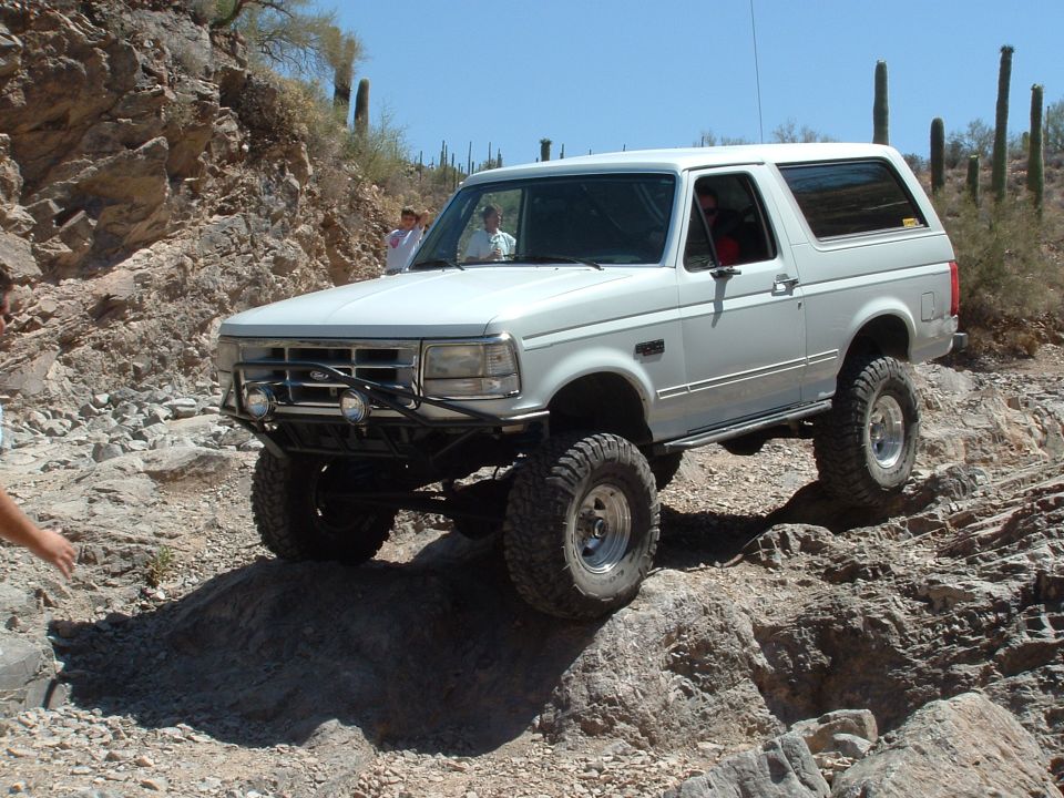 1990 Ford Bronco climbing over rocks on a desert trail with saguaro cacti in the background