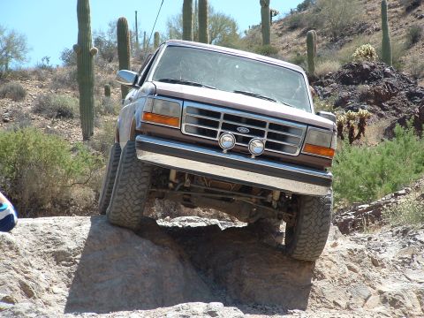 1990 Ford Bronco - Ford Bronco tackles a challenging rocky trail in a desert landscape.