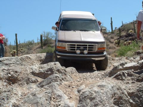 1990 Ford Bronco - A Ford Bronco navigates a rocky desert path under a clear blue sky.