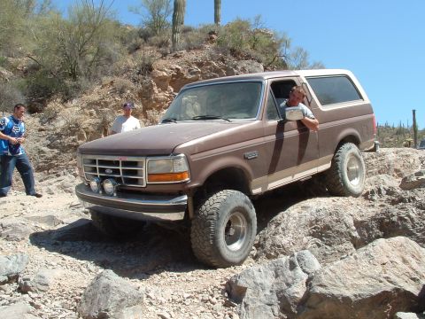1990 Ford Bronco - Brown 1990 Ford Bronco tackling a difficult off-road course in a desert landscape.