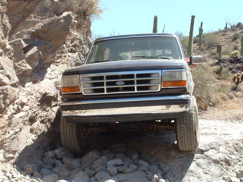 1990 Ford Bronco - A dark-colored Ford F-Series truck navigates a rocky, off-road path in a desert environment.