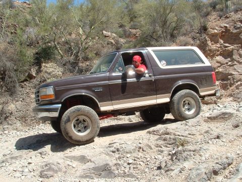 1990 Ford Bronco - A brown Ford Bronco navigates a rocky desert trail.