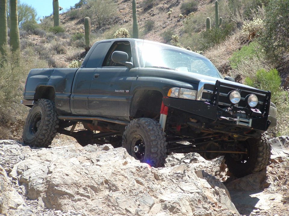 Dark green Dodge Ram 2500 off-roading on rocks, lifted suspension, winch on front bumper