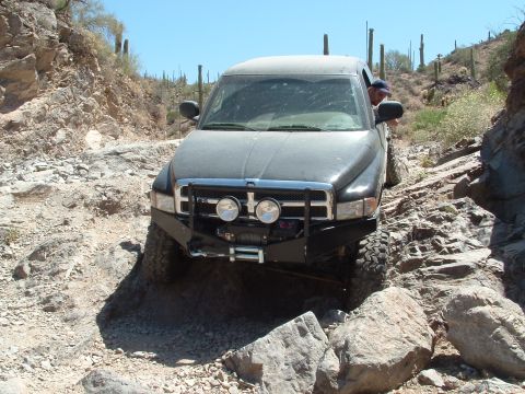1990 Ford Bronco - A driver navigates a rocky off-road trail in a modified Dodge Ram pickup truck.