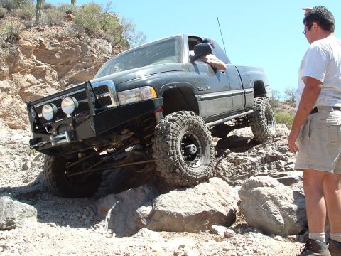 1990 Ford Bronco - A black pickup truck is shown off-roading on a sunny day.