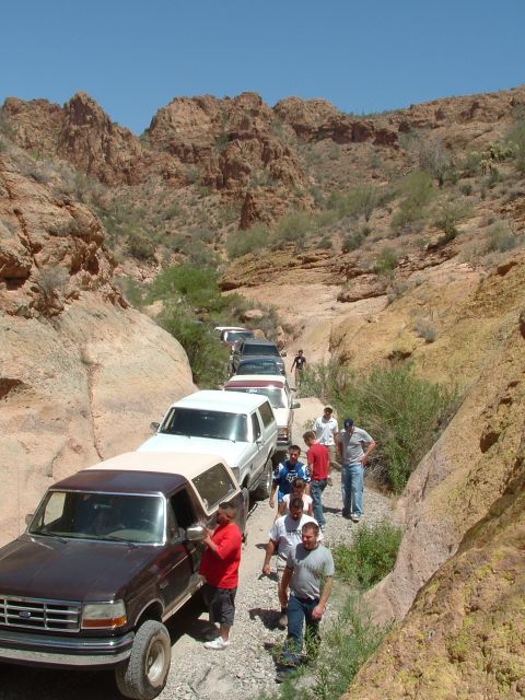 1990 Ford Bronco - A group of off-road vehicles navigate a narrow, rocky canyon under a clear blue sky.