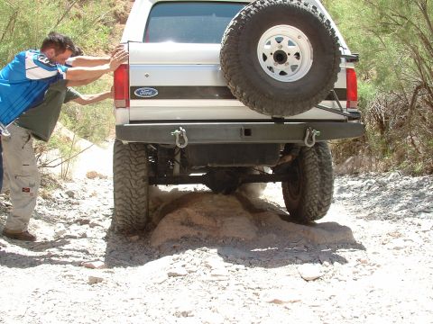 1990 Ford Bronco - Two men push a silver Ford Bronco as it navigates a difficult, rocky off-road path.