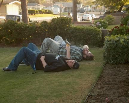 1993 Ford Taurus - Two men are seen lying on the grass, one holding a beer bottle, in a residential backyard setting.