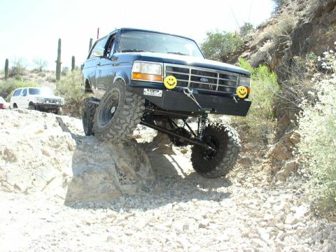 1993 Ford Bronco - A modified Ford Bronco tackles a challenging off-road course with a white SUV in the background.