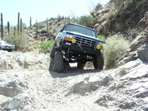 1993 Ford Bronco - A lifted 1993 Ford Bronco tackles a challenging off-road course in a desert landscape.