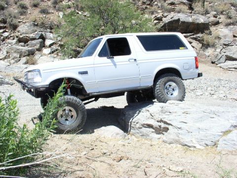 1993 Ford Bronco - A white Ford Bronco is shown off-roading on a rocky trail.