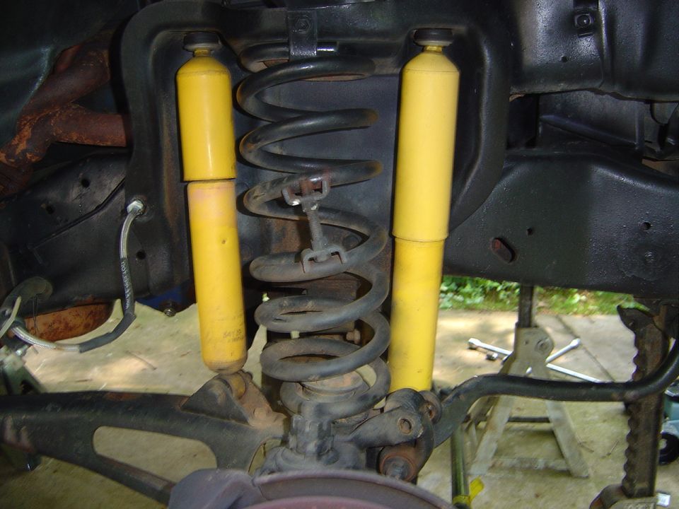 Underside suspension with black coil spring and two yellow shocks over concrete floor