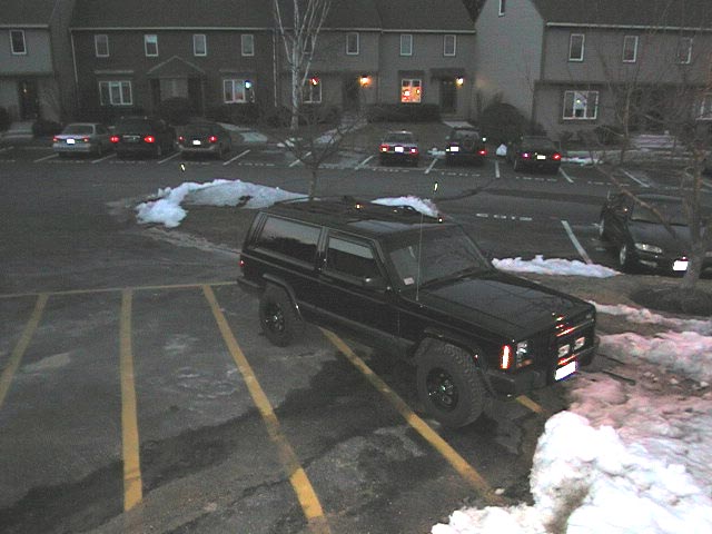 Black Jeep Cherokee parked in a snowy apartment lot at dusk