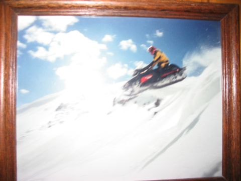 1986 Ford Bronco - A snowmobile rider takes flight on a steep, snow-covered mountain under a bright blue sky with scattered clouds.
