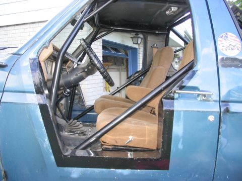 1986 Ford Bronco - The interior of a blue Ford Bronco features tan seats and a prominent black roll cage, suggesting off-road modifications.