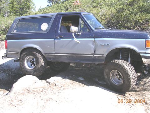 1994 Ford Bronco - A two-tone Ford Bronco navigates a rocky trail on a sunny day.