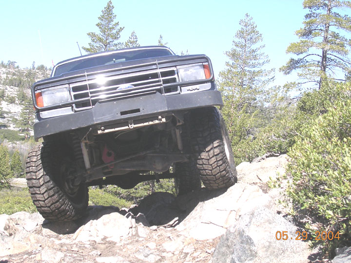Lifted dark blue Ford Bronco on mud tires flexing over granite rocks on a trail