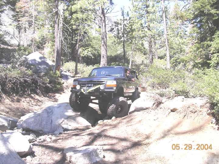 Dark blue lifted Ford Bronco climbing granite boulders on a forest trail