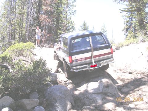 1994 Ford Bronco - A Ford Bronco navigates a rocky trail with a person standing on a hill in the background.