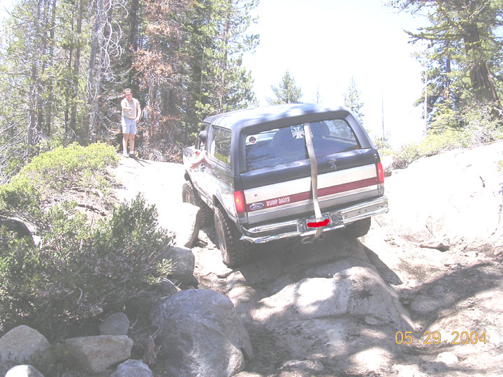 Dark gray Ford Bronco with red and white stripe on rear, driving over rocks