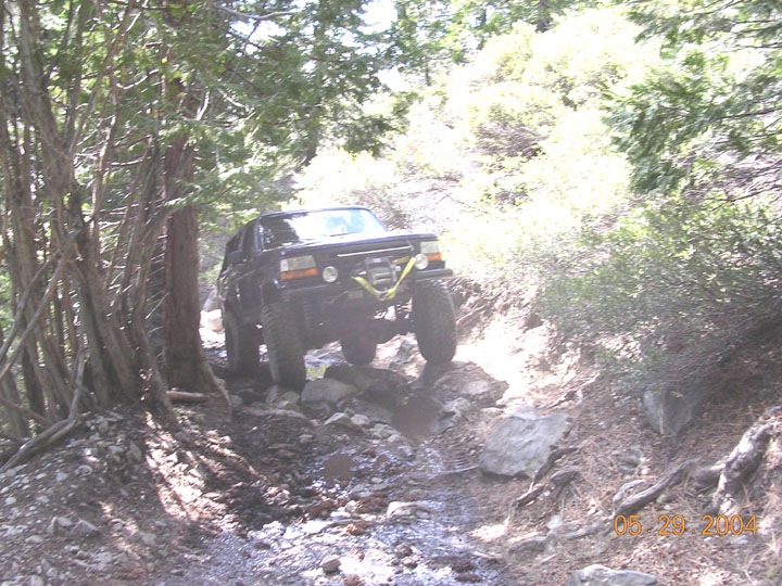 Black SUV driving over rocks on a wooded trail. It has a winch on the front