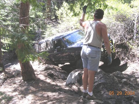 1994 Ford Bronco - A black SUV navigates a challenging off-road trail, with a person standing nearby.