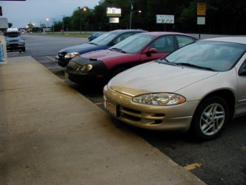 1997 Ford Taurus - Several cars are parked in a lot near a sidewalk, with trees and signs in the background.