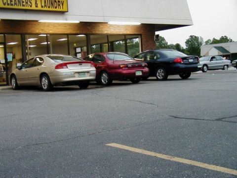 1997 Ford Taurus - Several sedans are parked in front of a commercial building with large windows.