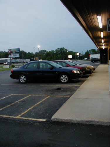 1997 Ford Taurus - A dark 1997 Ford Taurus is parked in a lot next to a building, with other vehicles visible behind it.