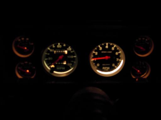 Backlit aftermarket speedometer, tachometer, and four small gauges glowing at night