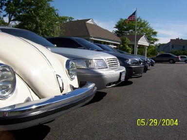 1999 Ford Crown Victoria - A lineup of vehicles is parked in a lot on a sunny day, with an American flag flying in the background.