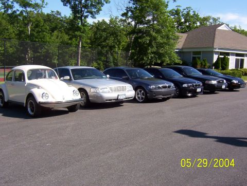 1999 Ford Crown Victoria - A collection of vehicles, including a classic Beetle and modern sedans, are parked in a row on a sunny day.