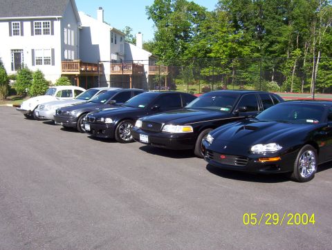 1999 Ford Crown Victoria - A row of cars including a black Ford Crown Victoria and a black Chevrolet Camaro.