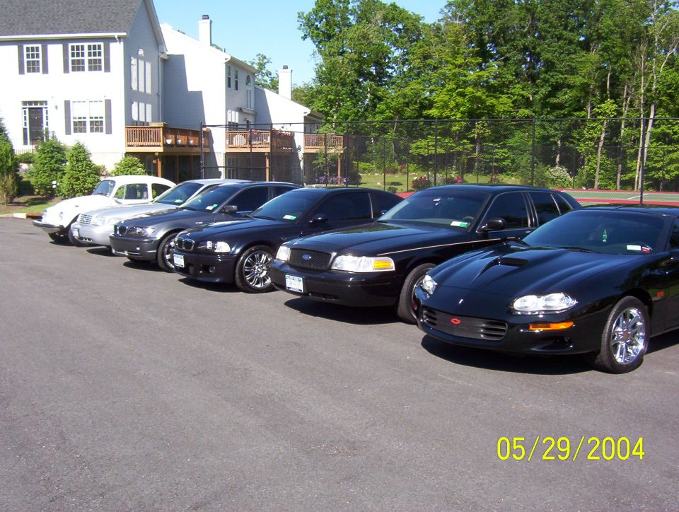 Several black cars and one white car parked in a line in front of a building