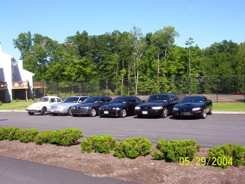 1999 Ford Crown Victoria - A collection of vehicles are parked in a lot with trees and a tennis court in the background.
