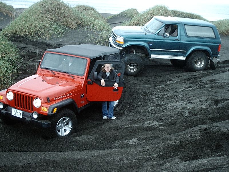 Green lifted Ford Bronco and red Jeep Wrangler Rubicon on black volcanic sand
