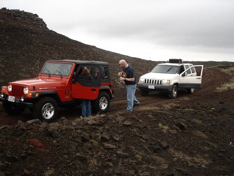 1996 Ford Bronco - Two Jeep SUVs stopped on a dirt path in a rocky, barren landscape under an overcast sky.