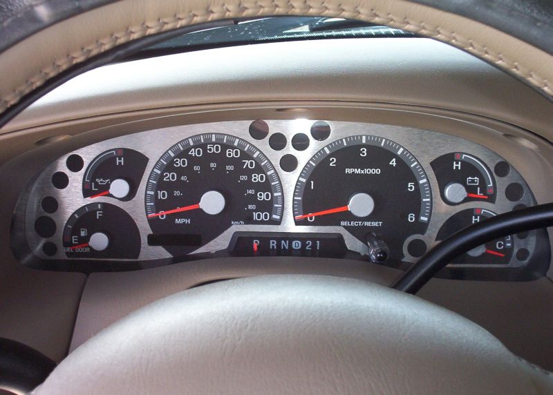 Brushed-metal gauge cluster with speedometer, tach and PRND21 indicator seen through tan steering wheel