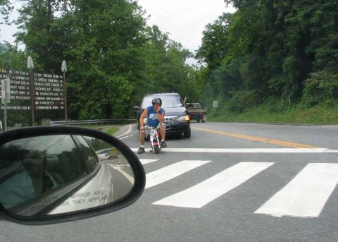 1995 Ford Bronco - A man on a mini-bike waits at a crosswalk in front of a black SUV.