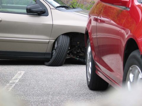1995 Ford Bronco - A tan car with a severely flat front tire is parked beside a red car on asphalt.